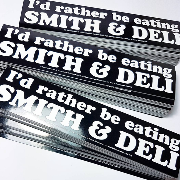 Stack of 'I'd rather be eating Smith & Deli' bumper stickers on a white background