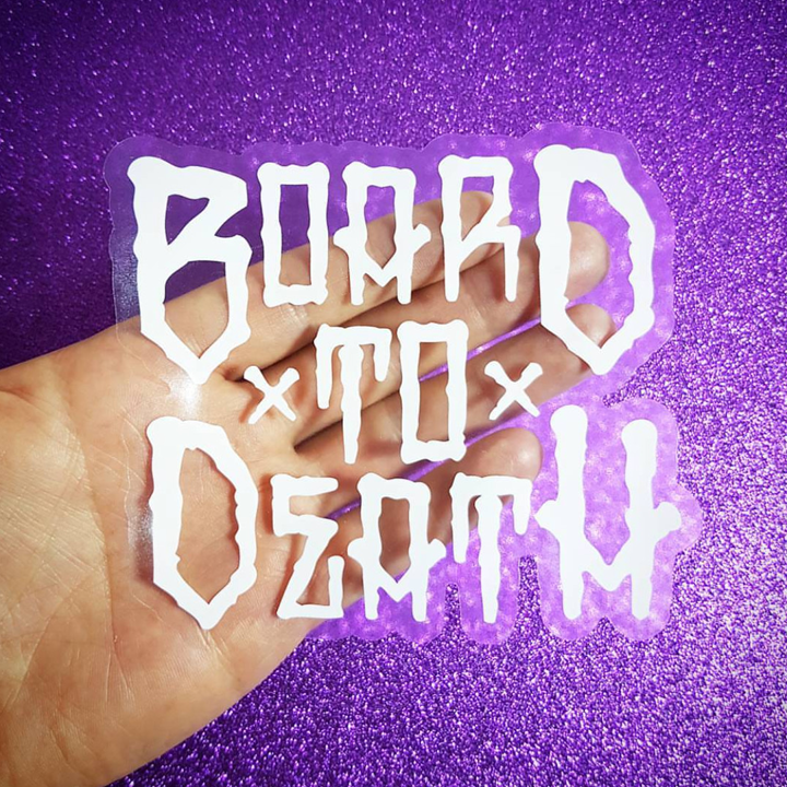 Hand holding a transparent sticker with 'Board to Death' text against a purple glittery background