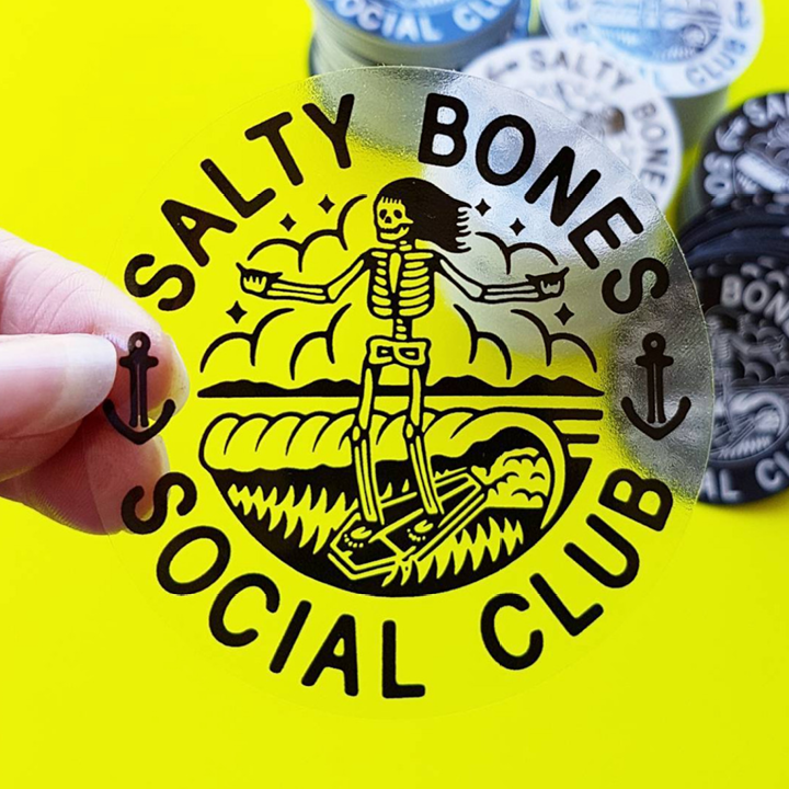 Salty Bones Social Club sticker held by a hand on a yellow background