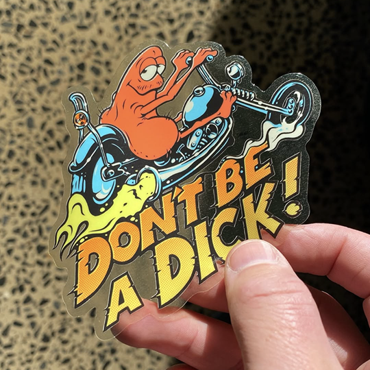 Sticker with cartoon character on a motorcycle and text 'DON'T BE A DICK!' held by a hand.