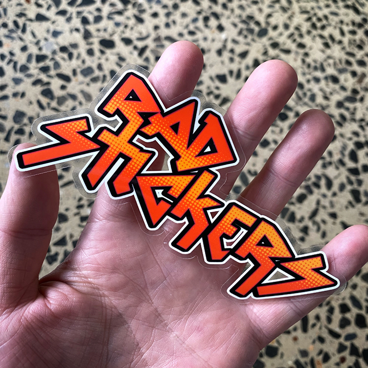 Hand holding a 'Rad Stickers' sticker against a patterned background