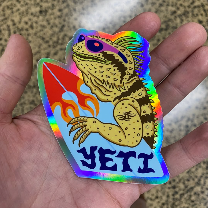 Holographic sticker of a creature labeled 'YETI' held in a hand.