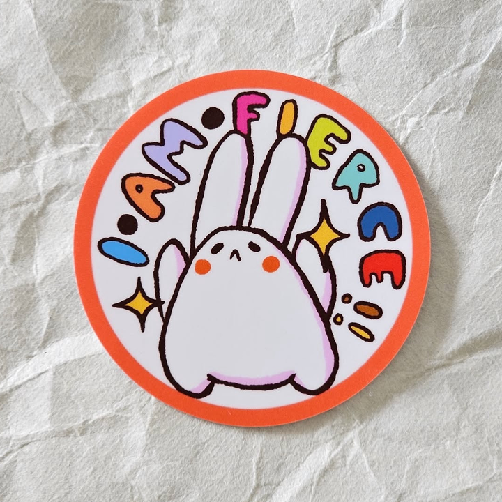 Circular sticker with a cartoon rabbit and colorful text on a textured light grey background