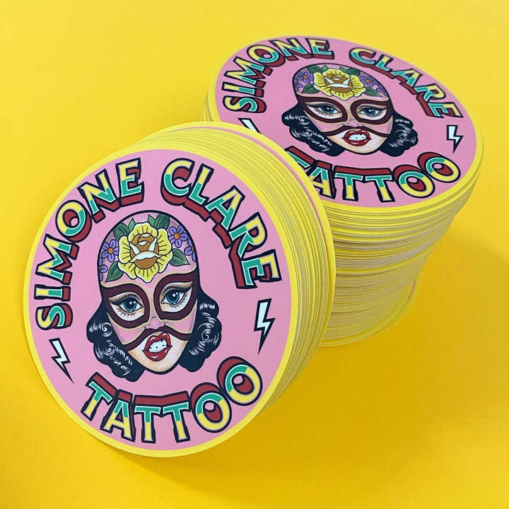 Stack of pink stickers with 'Simone Clare Tattoo' branding on a yellow background