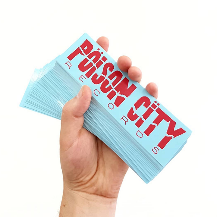 Hand holding a stack of 'Poison City Records' record stickers against a white background