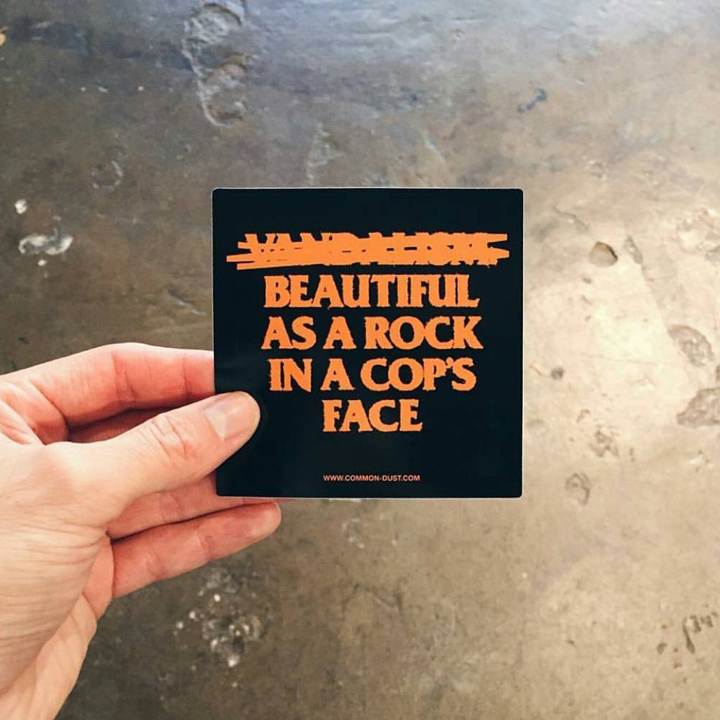 Hand holding a black sticker with orange text on a textured surface