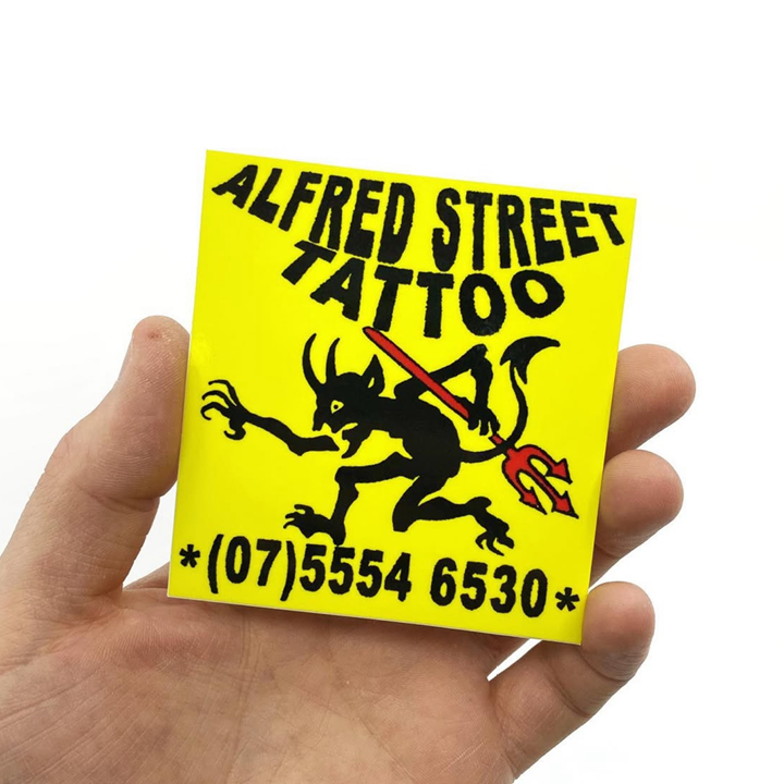 Hand holding a yellow stickers with 'Alfred Street Tattoo' logo and contact number.